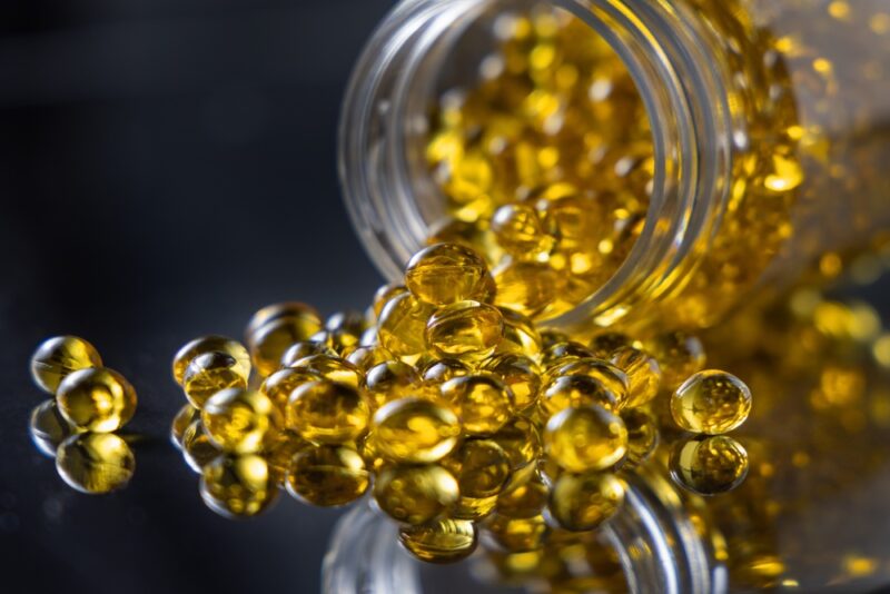 Kapsule omega 3 ribljeg ulja prosute iz bočice na tamnoj podlozi