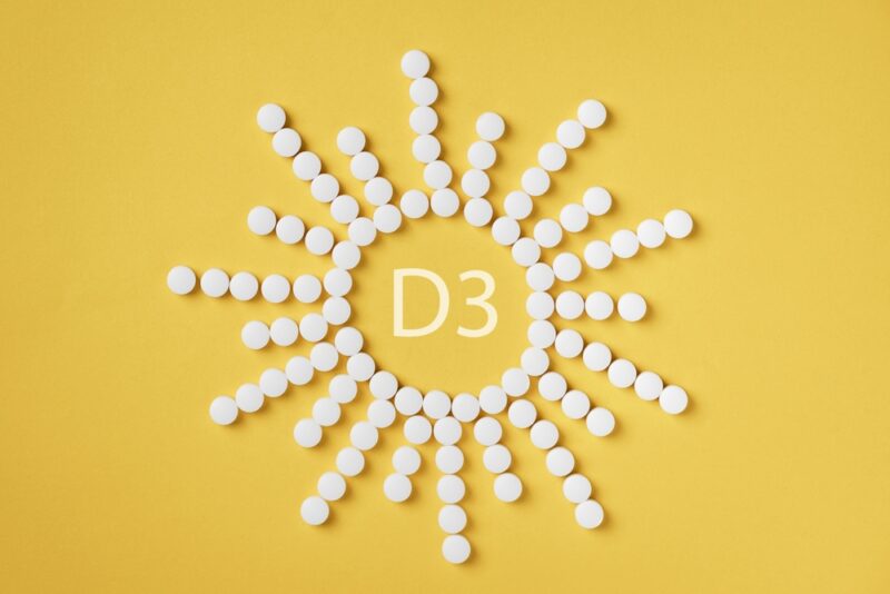 Tablete vitamina D3 raspoređene u obliku sunca na žutoj pozadini