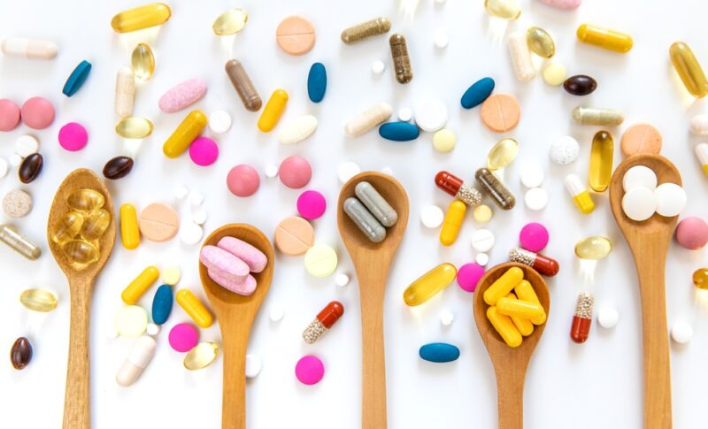 Različiti suplementi, vitamini i kapsule raspoređeni na beloj podlozi pored drvenih kašika